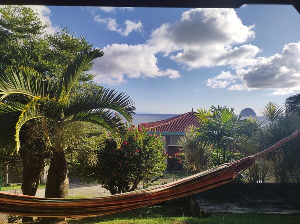Uma rede em um jardim exuberante, com vista para a área costeira e um edifício com telhado vermelho.