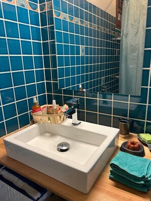Uma casa de banho com uma pia branca, azulejos azuis, um espelho e artigos de higiene no balcão.