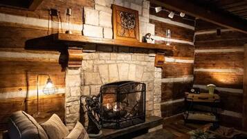 A log cabin interior with a stone fireplace, wooden walls, a sofa, and a table with a lamp.