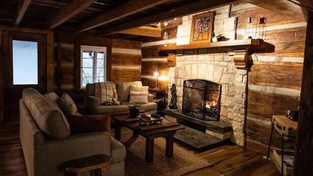A cozy log cabin interior with a stone fireplace, wooden furniture, and a rustic ambiance. - JuneBug Log Cabin, Nashville Music History, Dreamy Loft Suite, Stone Frpl. (Hendersonville)