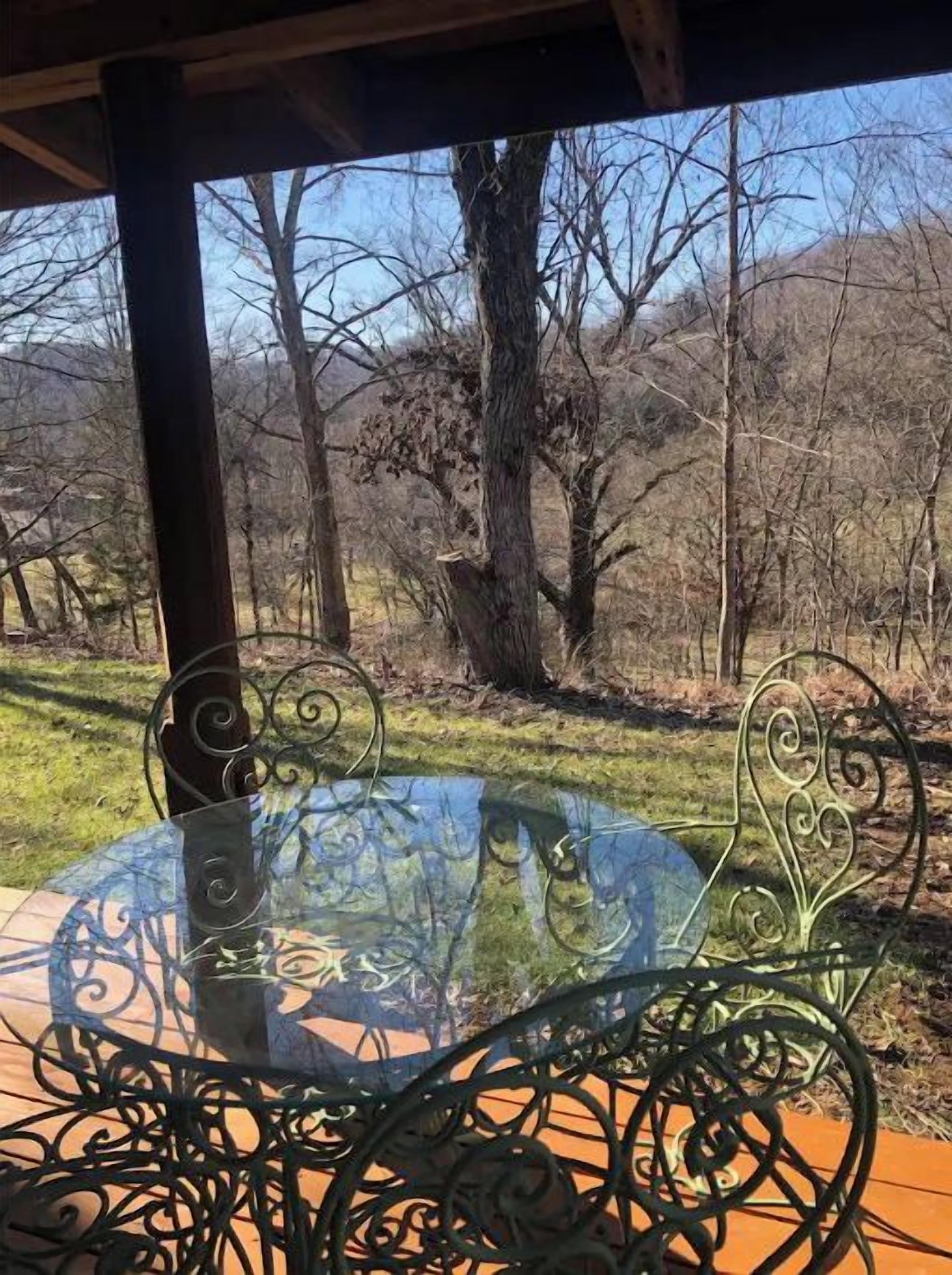 A round glass table with metal chairs in a covered outdoor area with a view of trees and hills.