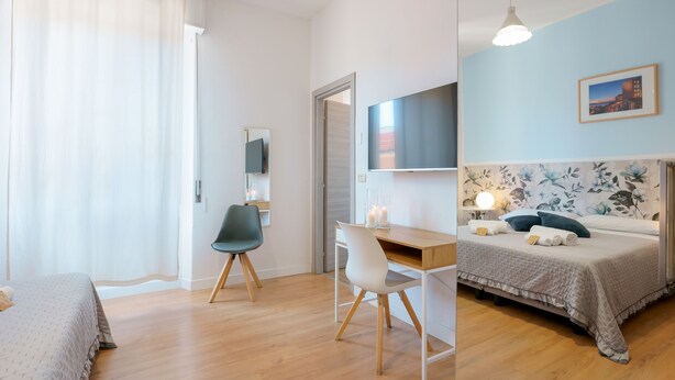 Un dormitorio moderno con cama, escritorio, silla, televisor y un cuadro en la pared.