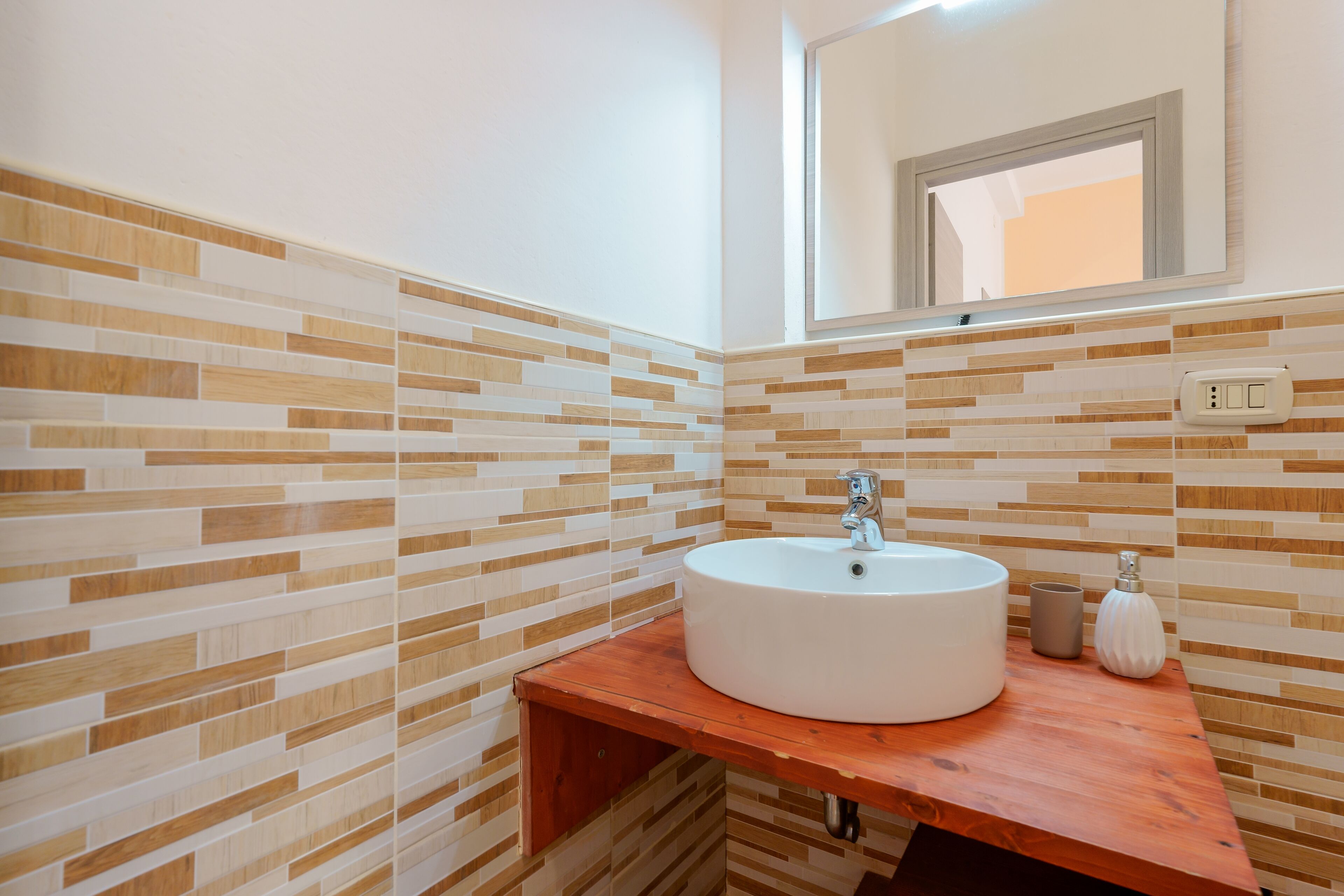 A bathroom with a tiled wall, a round sink, and a wooden countertop.