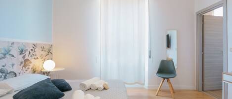A modern hotel room with a bed, a chair, a small table, and a mirror.