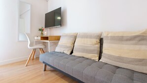 Una sala de estar moderna con un sofá gris, un escritorio blanco y un televisor de pantalla plana montado en la pared.