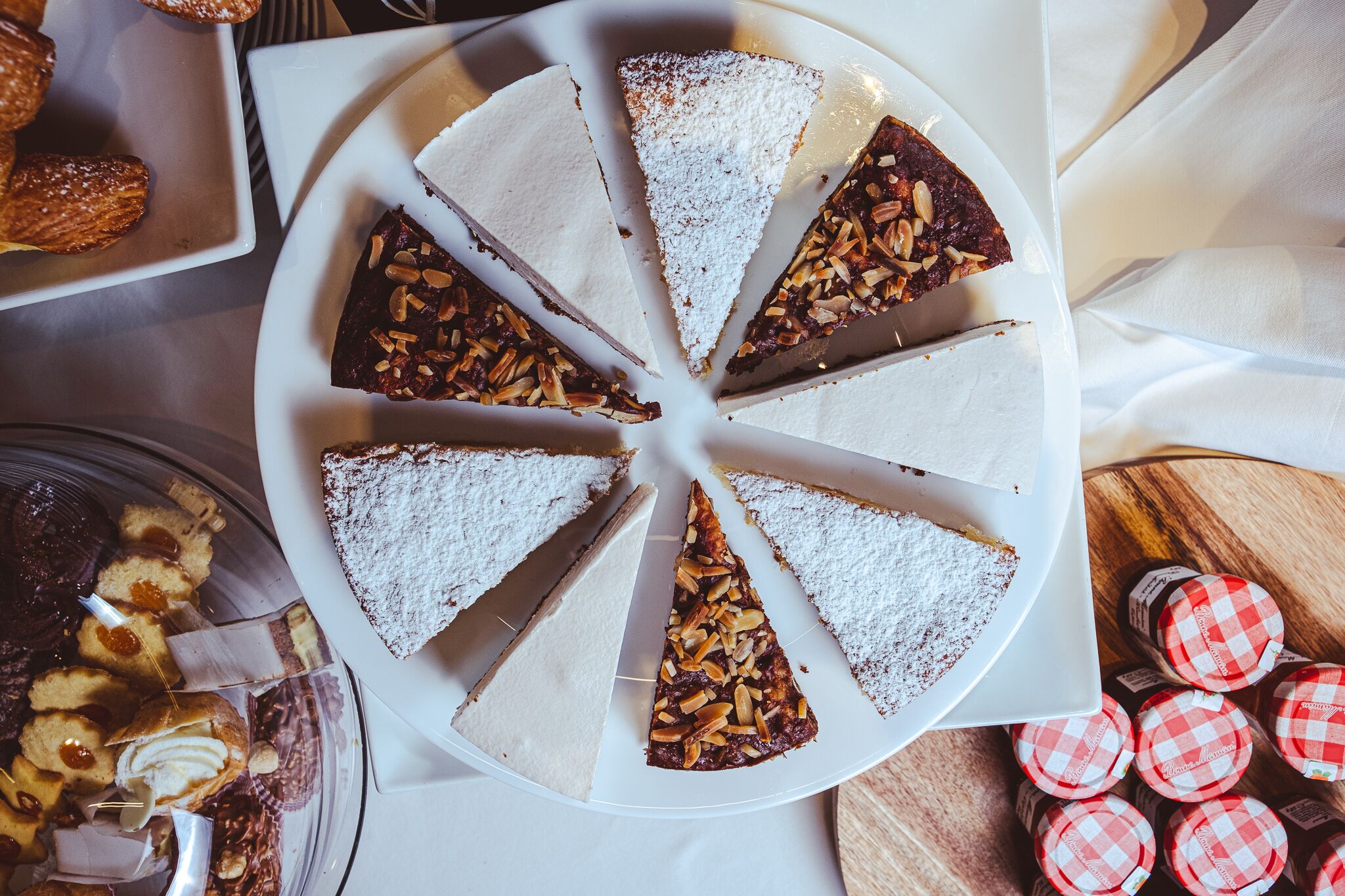 Ein runder, weißer Teller mit dreieckigen Kuchenstücken, einige mit Mandeln, andere mit Puderzucker bestreut.