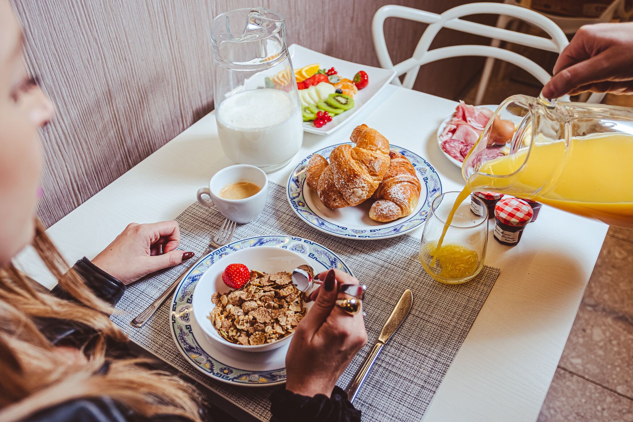 A breakfast table with croissants, fruit, cereal, milk, and orange juice.