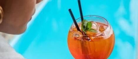 A person holding a cocktail with a pool in the background.