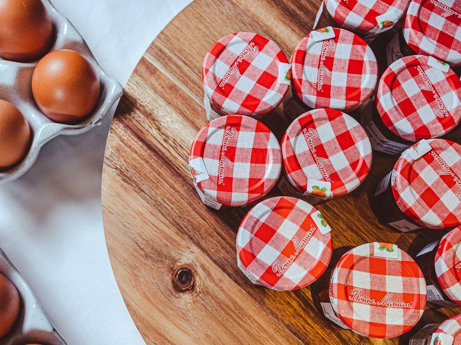 A wooden board with red and white checkered lids, a carton of brown eggs, and a white cloth.