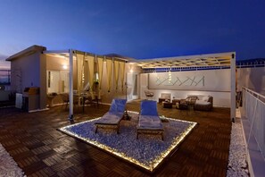 Eine moderne Außenpatio mit zwei Loungesesseln, einem Holzboden und einer dekorativen Lichtinstallation.