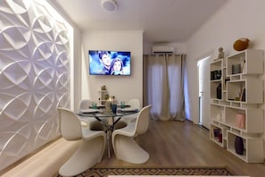 Ein modernes Wohnzimmer mit Essbereich, einem an der Wand montierten Fernseher und einem Bücherregal.