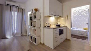 A compact living space with a kitchenette, built-in shelving, and a bed with a geometric-patterned headboard.