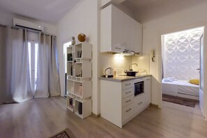 Ein kompakter Wohnraum mit Küchenzeile, eingebauten Regalen und einem Bett mit geometrischem Kopfteil.