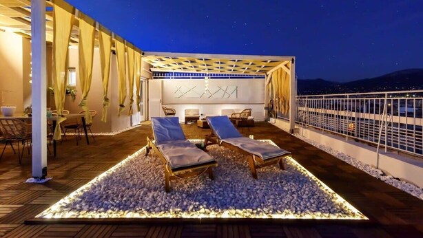 A rooftop terrace with two lounge chairs, a seating area, and a view of the city at night.