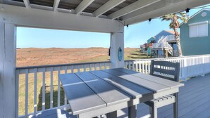 Eine Terrasse im Freien mit Tisch und Stühlen, mit Blick auf eine grüne Landschaft und ein Haus mit blauer Fassade.