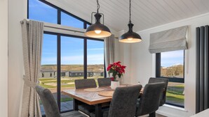 Ein Essbereich mit Tisch und Stühlen, großen Fenstern und Blick auf die Landschaft.