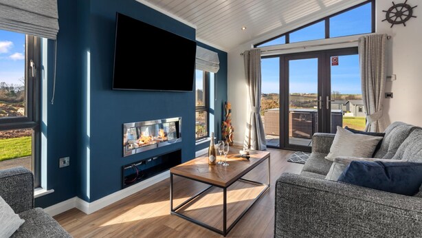 Ein modernes Wohnzimmer mit großem Fernseher, Kamin und Blick ins Freie.