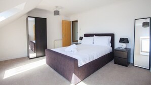 Une chambre à coucher avec un grand lit, une table de chevet, un miroir et une porte donnant sur une autre pièce.