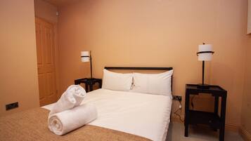 A hotel room with a bed, two bedside tables, a lamp, and a rolled towel on the bed.