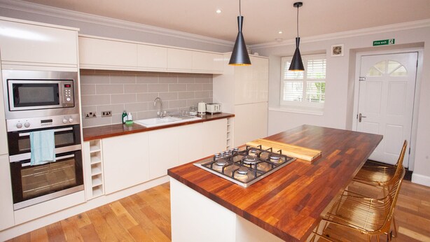 A modern kitchen with a central island, built-in oven, microwave, and gas stove. - Stylish West End Flat in Glasgow (Glasgow City)