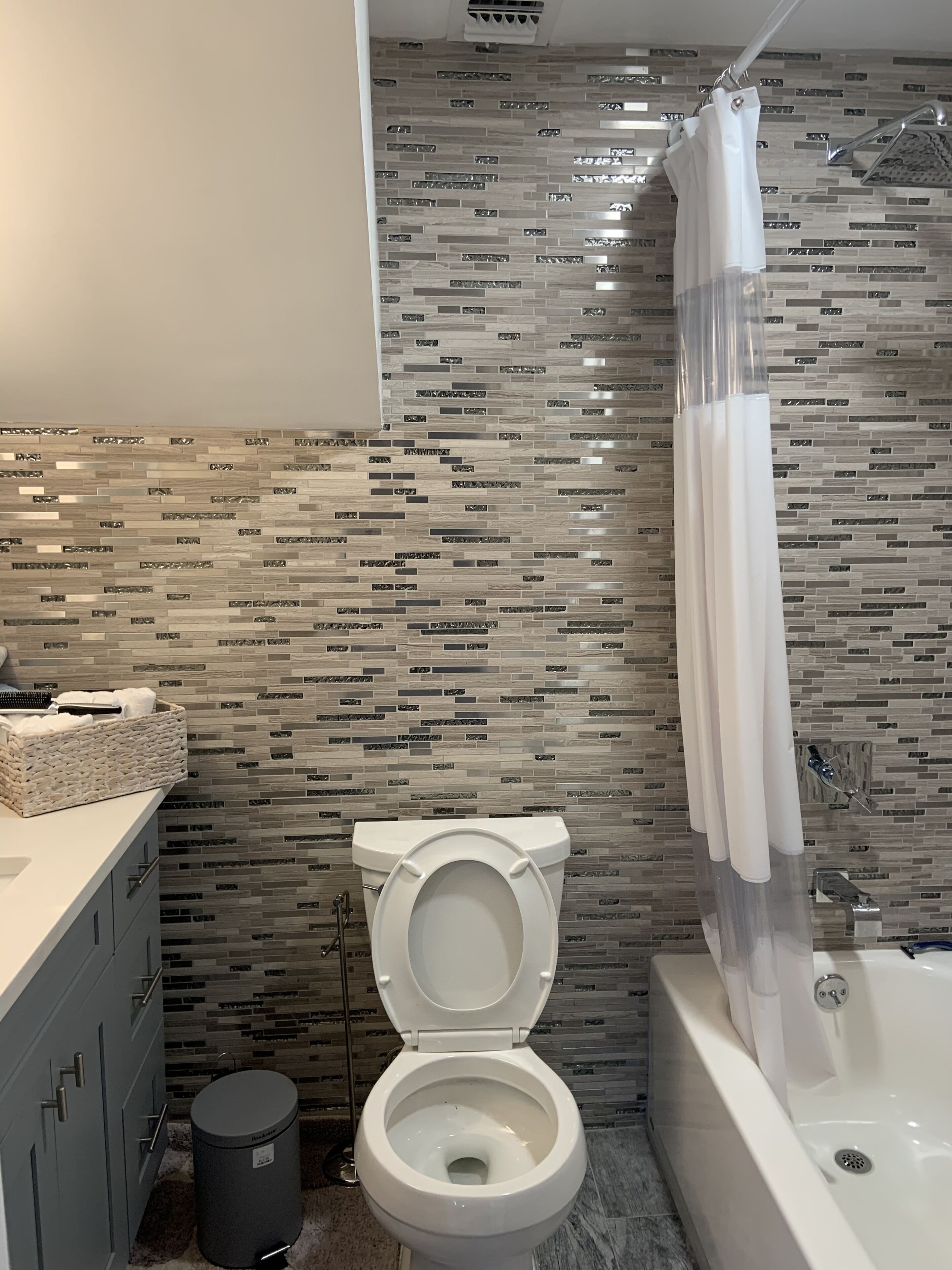 A modern bathroom with a tiled backsplash, a toilet, a bathtub, and a shower curtain.