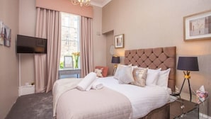 A hotel room with a large bed, a television, a window with curtains, and a chandelier. - Charming 3-Bedroom Retreat in Glasgow West End (Glasgow City)