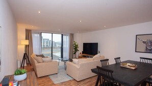 A modern living room with a sofa set, a dining table with chairs, a flat-screen TV, and a large window offering a city view.