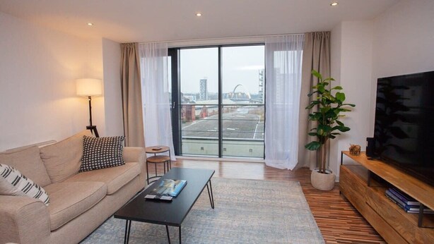 A modern living room with a sofa, coffee table, TV, and a large window with curtains.