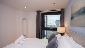 A hotel room with a bed, a window with curtains, a lamp, and a painting on the wall.