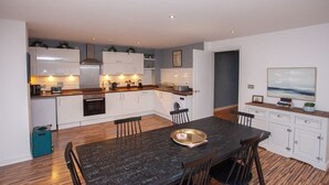 A modern kitchen with white cabinets, a dining table, and a large window.