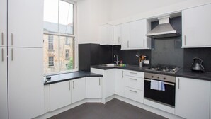 A modern kitchen with white cabinets, a black countertop, a gas stove, and a window providing a view of the outside. - Spacious, 4 Bed Flat Overlooking Park in West End (Glasgow)