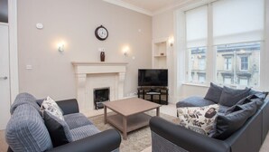 A living room with a fireplace, sofa, television, and large windows. - Spacious, 4 Bed Flat Overlooking Park in West End (Glasgow)