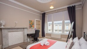 A hotel room with a bed, a desk, a chair, a fireplace, and a window with curtains. - Spacious, 4 Bed Flat Overlooking Park in West End (Glasgow)