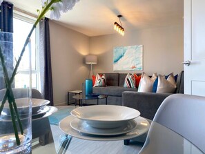Un salon moderne avec un canapé, une table à manger avec de l’assiette, une lampe et un tableau au mur.