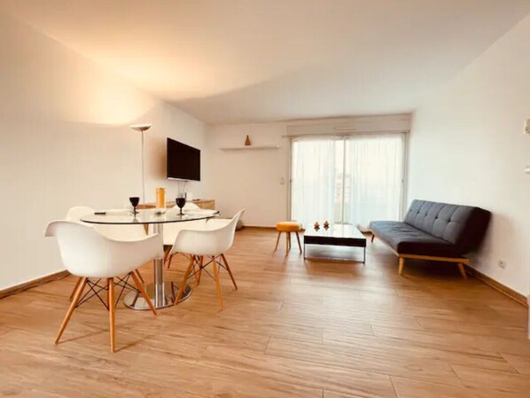 A modern living room with a dining area, a sofa, and a flat-screen TV.