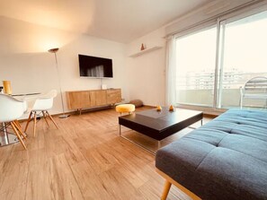 A modern living room with a sofa, a coffee table, a TV, and a dining area with chairs and a table.