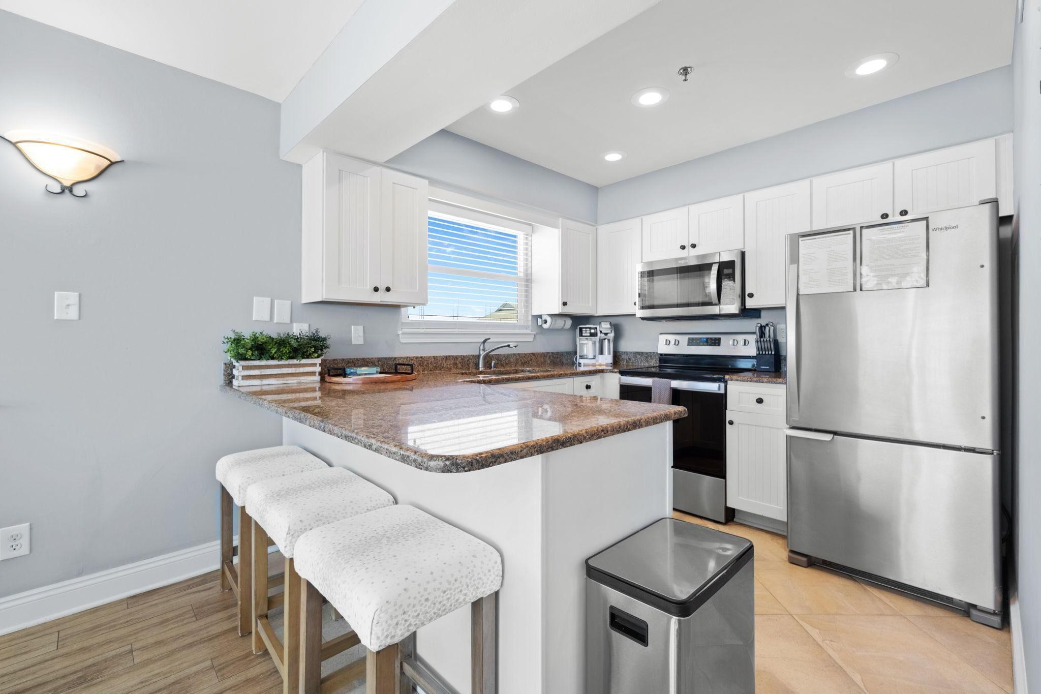 A modern kitchen with white cabinets, a granite countertop, stainless steel appliances, and a small island with bar stools.