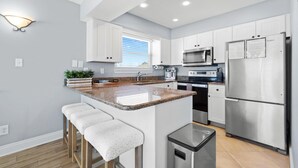 Cocina moderna con armarios blancos, encimera de granito, electrodomésticos de acero inoxidable y una pequeña isla con taburetes de bar.