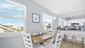 Una cocina moderna con armarios blancos, una mesa de comedor de madera y vistas de la ciudad a través de amplios ventanales.