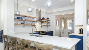 Une cuisine moderne dotée d’un îlot central, de tabourets de bar, de luminaires suspendus et d’étagères intégrées.