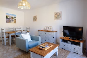 A living room with a sofa, dining table, chairs, a TV, and a cabinet.