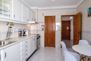 A compact kitchen with white cabinets, a stainless steel sink, and a dining area with white chairs.