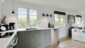 A modern kitchen with white wooden paneling, a large island with grey drawers, a built-in oven, and a window with a view of greenery.
