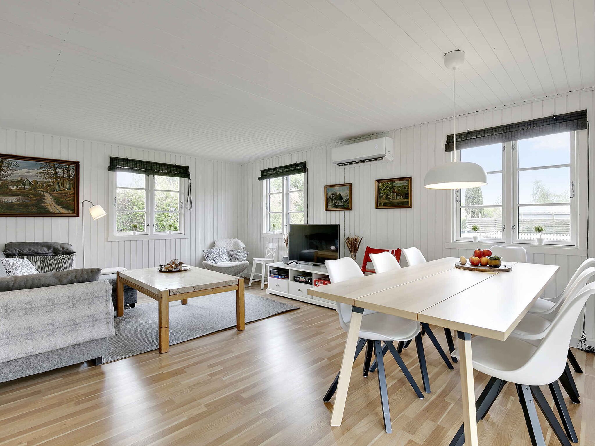 Een ruime woonkamer met een eethoek, witte muren, houten vloeren en grote ramen.