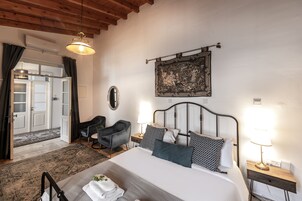A hotel room with a bed, bedside tables, a chair, a rug, a painting, and a door.