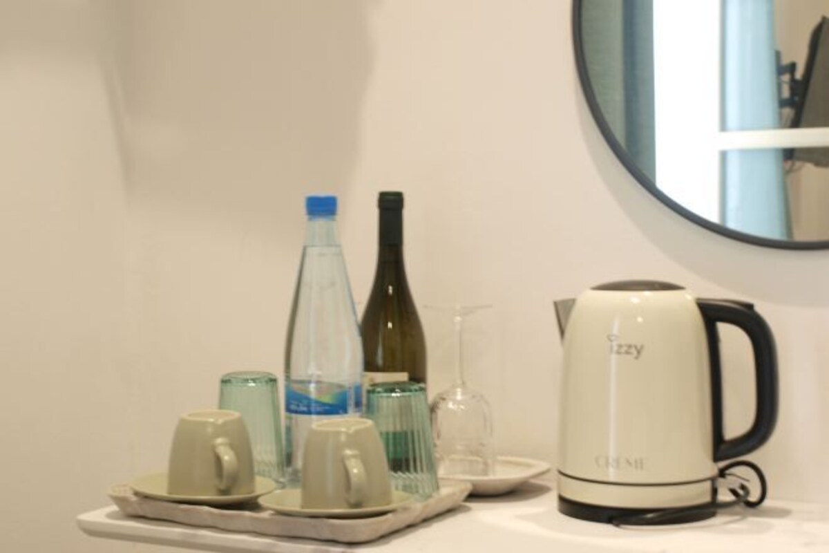 A kitchenette with a coffee maker, a water bottle, a wine bottle, and a glass.