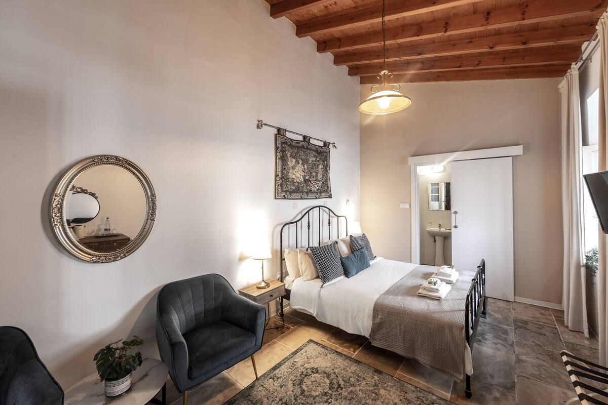 A bedroom with a bed, bedside table, lamp, chair, and a large mirror.