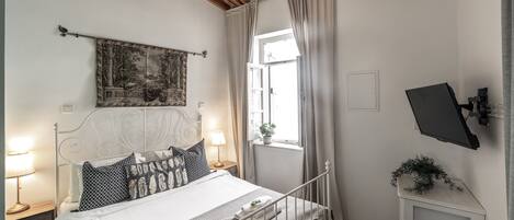 Une chambre bien rangée, avec un lit, des tables de chevet, un téléviseur fixé au mur et une fenêtre avec des rideaux.