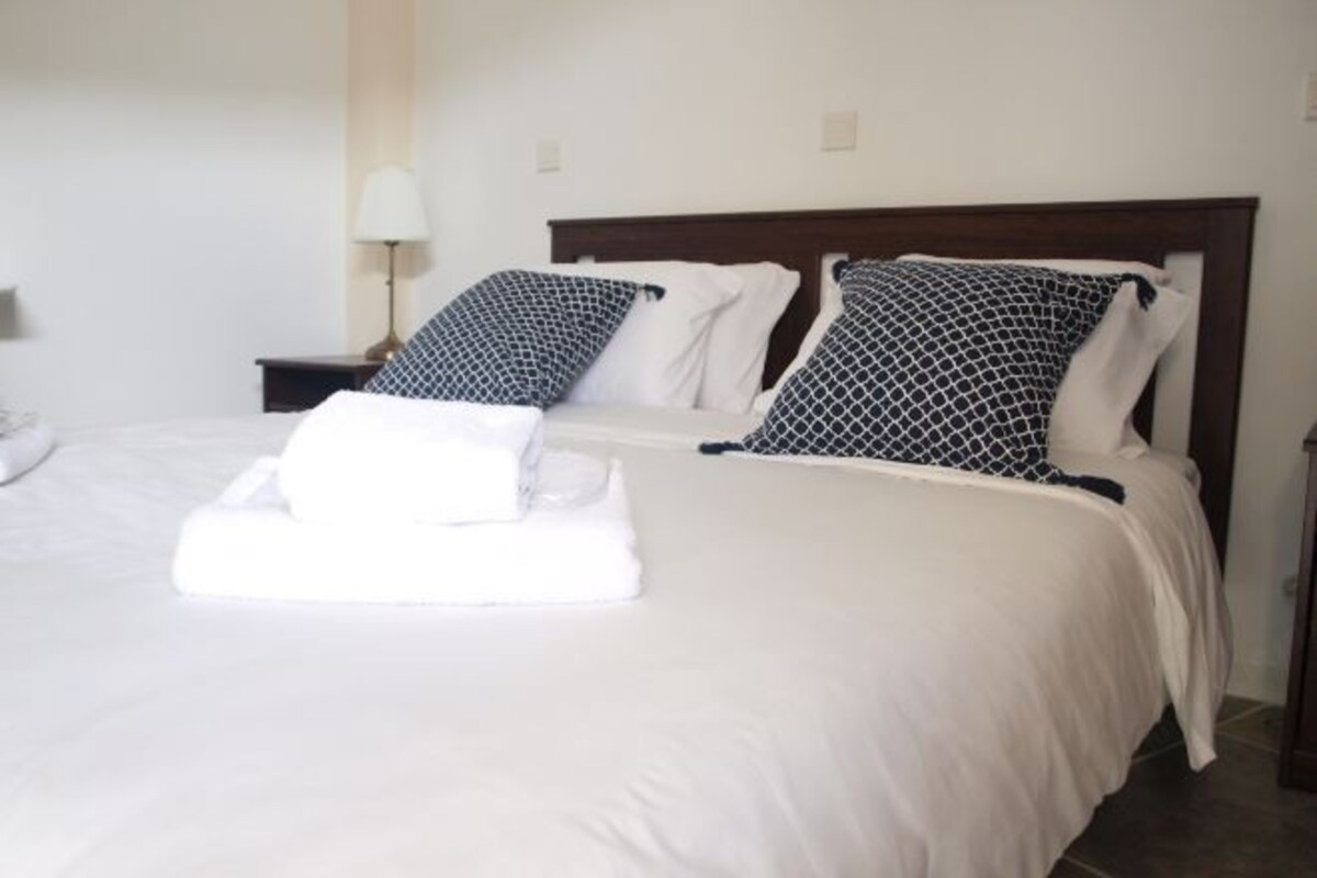 A neatly made bed with white bedding and two patterned pillows, a bedside lamp, and a folded white towel on the bed.