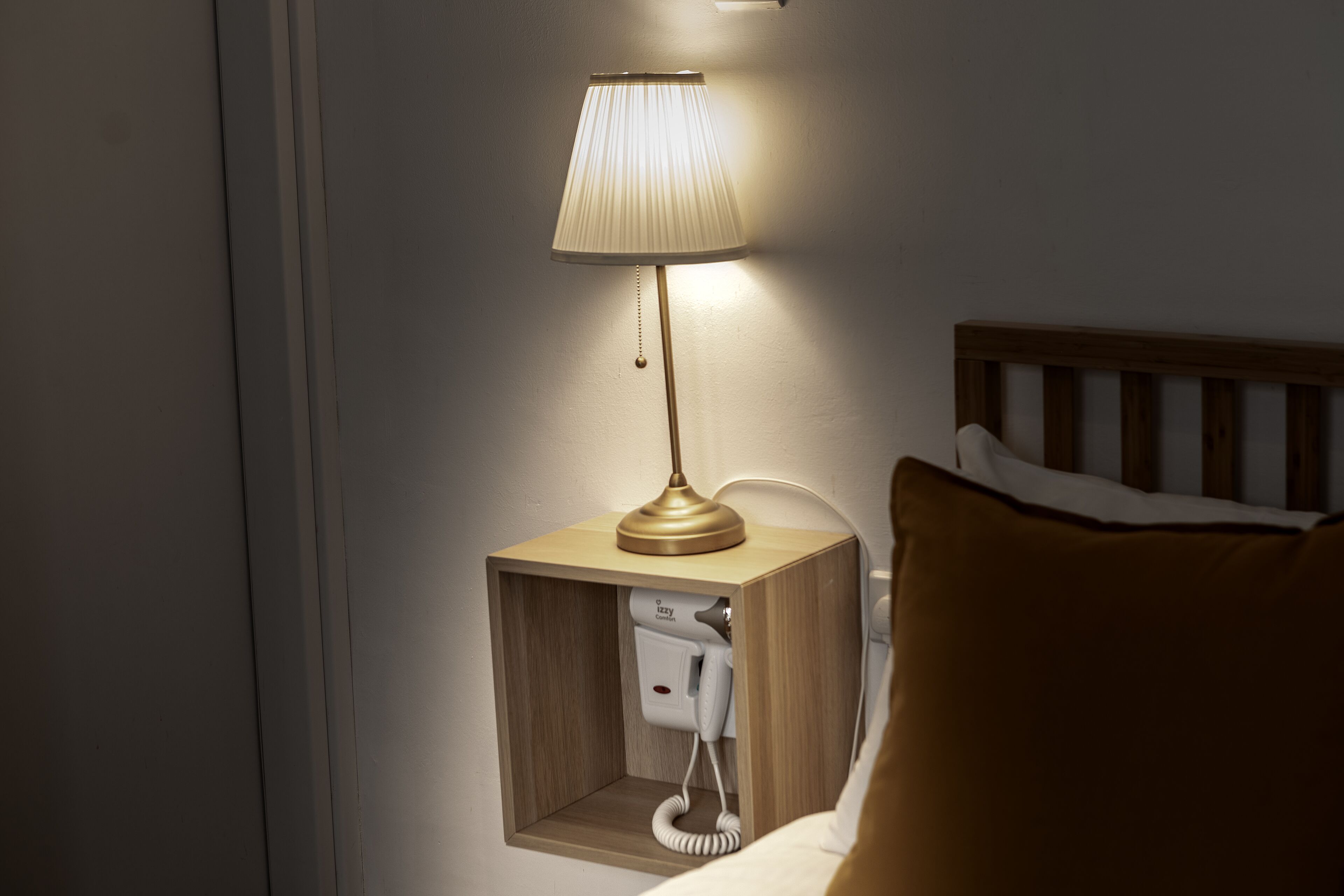 A bedside table with a lamp, a phone, and a wooden headboard.